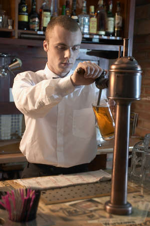 young barman at a bar counter pouring beerの写真素材