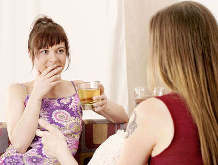 two girls, young women chatting on a sofa and drinkingの写真素材