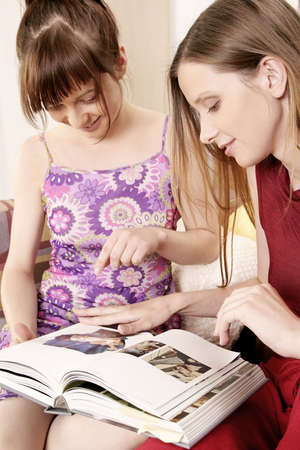 two girls, young women sitting on a sofa and watching photo-album