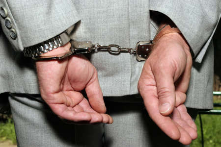 Arrested man in a business suit - hands in cuffs - close up の写真素材