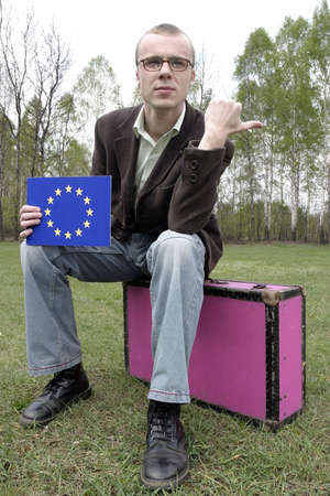Student hitch-hiking with a european union sign on a board and sitting on a suitcase.の写真素材