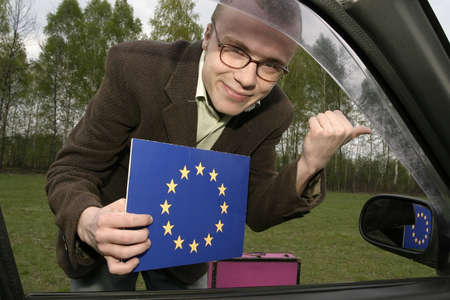 Smiling student hitch-hiking with a european union sign on a board and a suitcase.の写真素材