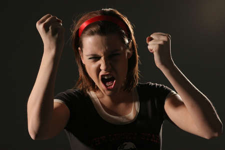 Young angry woman in a deep shadow screaming on a black background.の写真素材