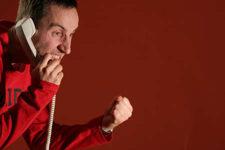 Young man in a red pullover screaming on the phone - isolated  background.の写真素材