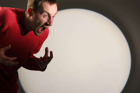 Young man in red pullover screaming and gesticulating - with a white circle in the background.の写真素材