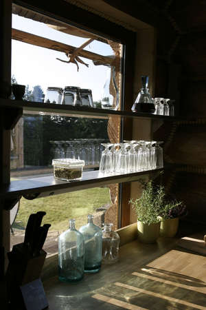 Empty stylish glasses and bottles on a shelf at a window in country side house.の写真素材
