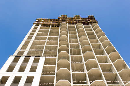 Facade of a modern monolithic residential building against the blue sky. Unfinished construction of...