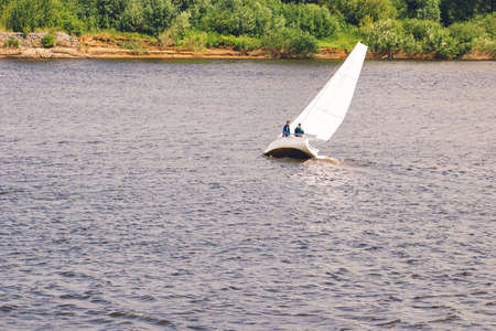 Yacht with white sails at Volga river. Sailboat tilted in a gust of wind. Boat with a sail is sinking.の写真素材