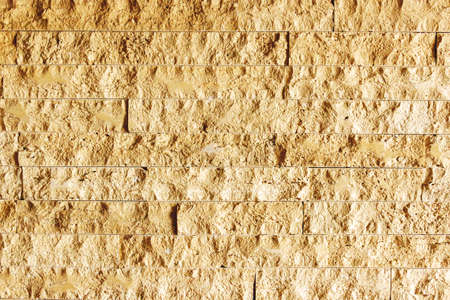 The wall of travertine. Beige brick wall with chipped facade illuminated by side light.の写真素材