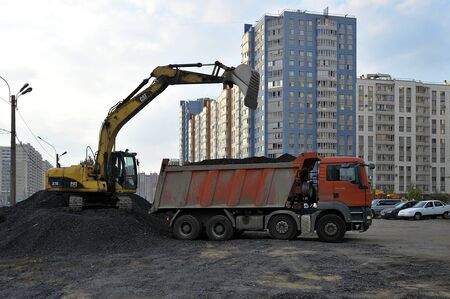 St. Petersburg, Russia - 19 SEPTEMBER: yellow excavator loads ib a red truck black gravel on SEPTEMBER 19, 2014, St. Petersburg, Russiaのeditorial素材