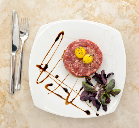 Steak Tartar. Ground beef and raw egg with herbs and spices on a marble background, top viewの写真素材