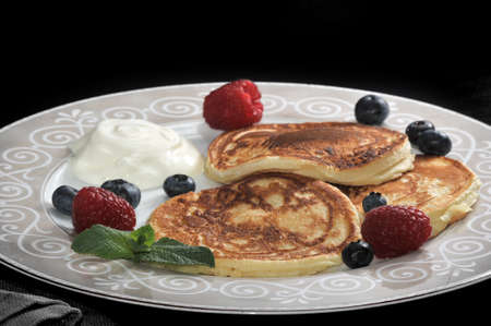 pancakes with sour cream on the plate with raspberries and blueberries and a mint leaf.