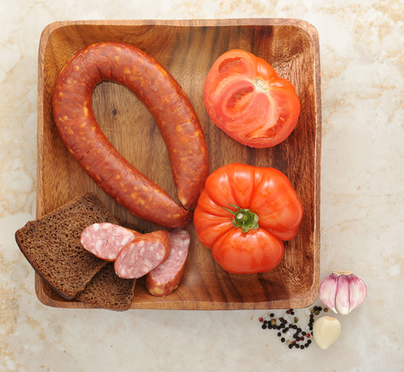 Krakow sausage, tomatoes and black bread on wooden plate. top viewの写真素材