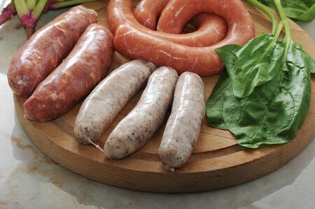 raw sausages for a barbecue with spinach leaves on wooden plate.の写真素材