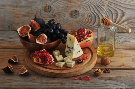 figs and black grapes in a wooden bowl, cheese, pomegranate, honey and walnutsの写真素材