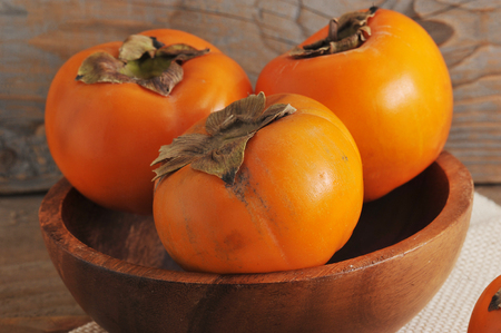 whole  orange persimmon in a wooden plate on canvasの写真素材