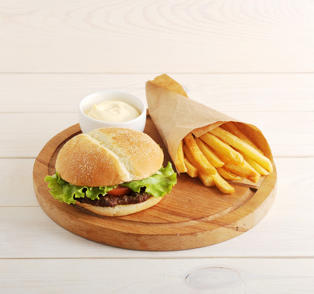fried potatoes in a paper bag, cheese sauce and hamburger on wooden backgroundの写真素材