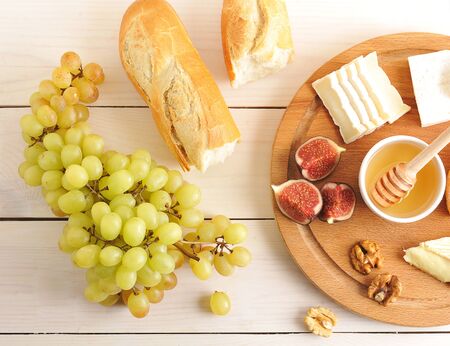 continental Breakfast - cheese, honey, figs, walnuts, grapes and baguette on wooden Board - top viewの写真素材