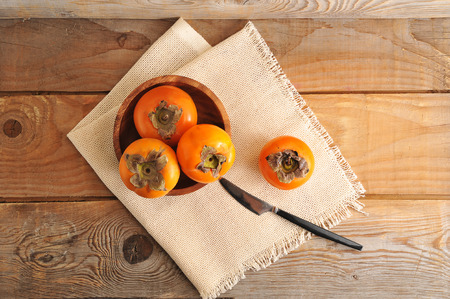 whole  orange persimmon in a wooden plate on canvasの写真素材