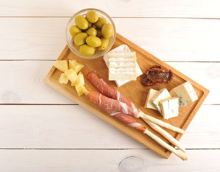 bacon on bread sticks, cheese, dried tomatoes, olives on a wooden Board on wooden background - top viewの写真素材