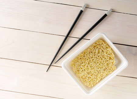 Dry noodles in a plastic bowl before pouring water with chopsticks on wooden background - top viewの写真素材