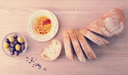 fresh bread, cut into slices with olives and olive oil with balsamic vinegar in a bowl on wooden background - top view in vintage aged styleの写真素材