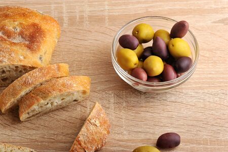 olives yellow and purple in the transparent plate and bread ciabatta with olives on wooden...