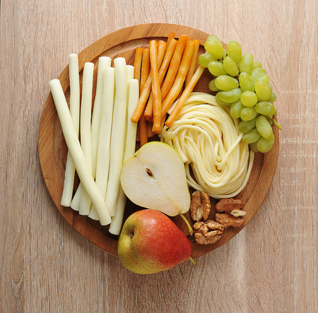 various types of cheese Suluguni cheese on a wooden plate with grapes, pear and walnuts - top view