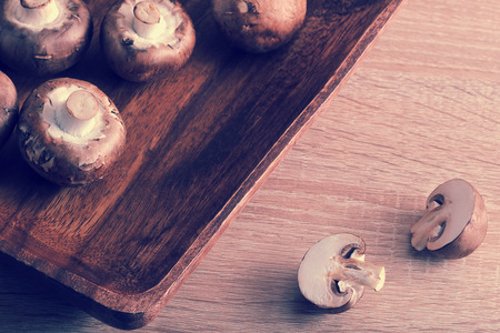 Fresh raw brown chestnut mushrooms whole in wooden plate and slised mushrooms on wooden background - view in vintage aged styleの写真素材