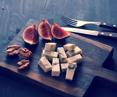 Blue cheese, fresh figs and walnuts on a wooden Board and a knife and fork on a black wooden rustic backgroundの写真素材