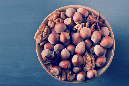 Nuts in bowl - hazelnut in shell, peeled walnuts, anise on dark rustic wooden background - top view