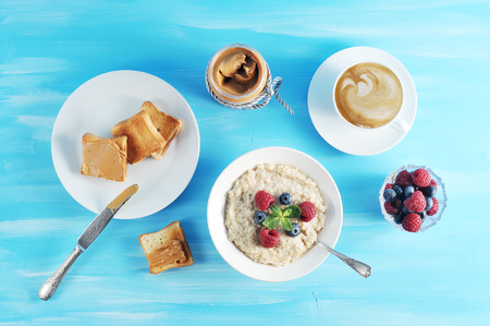 Breakfast oatmeal porridge on a blue background, oatmeal with berries, toast with peanut butter and...