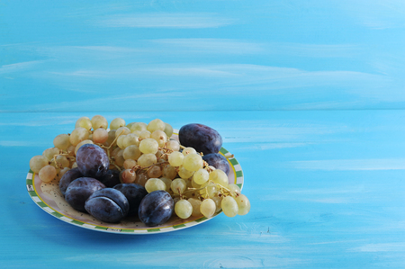 fruit plate plums and grapes in a bowl on a blue wooden background の写真素材