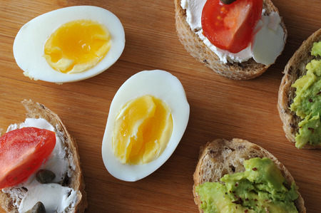 canape sandwiches on a wooden Board - avocado sandwiches, cheeses, tomatoes, eggs and capers - top...
