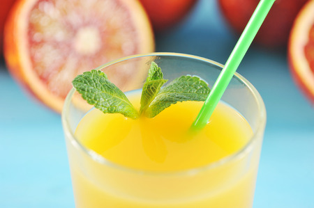 orange juice in glass with mint and a straw on a background of ripe juicy blood oranges on a blue backgroundの写真素材