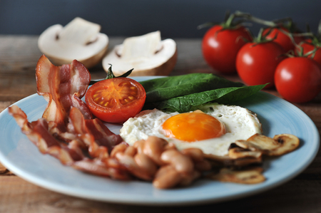 Breakfast of eggs with bacon, beans, mushrooms, tomatoes and spinach - on a wooden Boardの写真素材