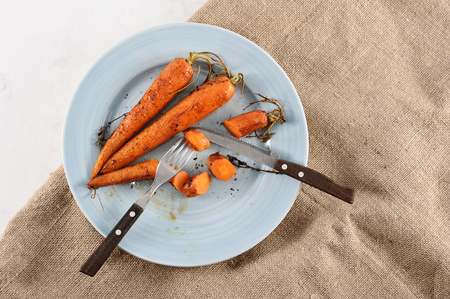 stewed carrots with honey, whole and cut into pieces on a blue plate with Cutleryの写真素材