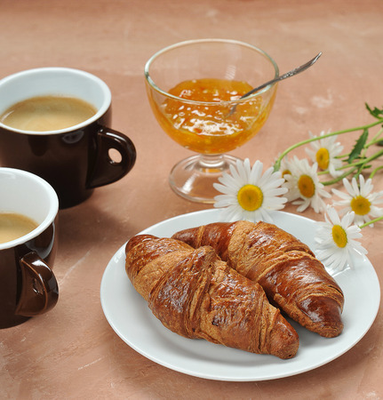 morning coffee and croissants, two cups of coffee, jam and daisies on a brown backgroundの写真素材