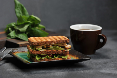 square sandwich with chicken breast on a plate on a dark background and coffee mug