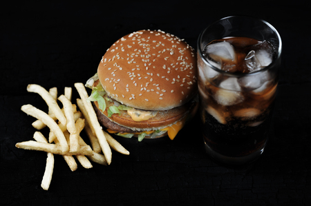 burger with french fries and a glass with ice  on a black rustic backgroundの写真素材