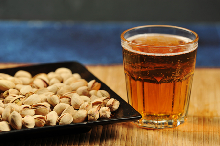pistachios in a plate and a glass of beer on a dark backgroundの写真素材
