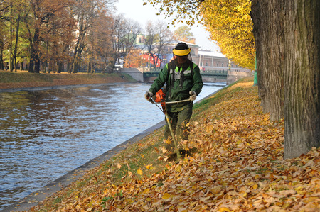 St.-Petersburg, Russia - October 18, 2018:a worker mows grass with a petrol scythe near mikhailovsky park in st. petersburgのeditorial素材