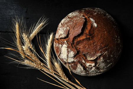 rye bread, whole loaf and ears on dark rustic background