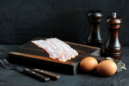 bacon on wooden Board and eggs, Cutlery on black backgroundの写真素材