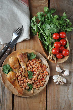 fried chicken legs with beans and tomatoes on a wooden plate top viewの写真素材