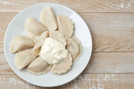 dumplings with sour cream on a plate on a wooden background-top viewの写真素材