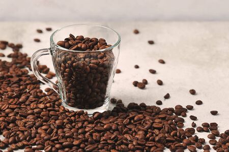 coffee beans in a transparent glass mug on a background of coffee beans scattered on a concrete background の写真素材