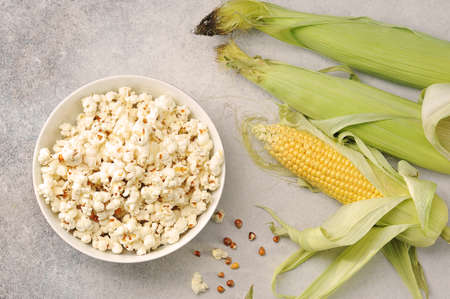 ears of corn and prepared popcorn in a bowl on a gray background - top viewの写真素材