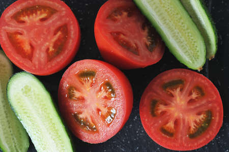 red tomatoes and cucumbers cut into halves - top view flat layの写真素材