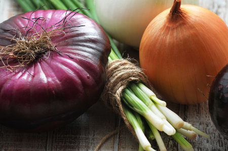 different varieties of onions - green, yellow, white and red onions on a wooden background